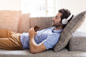 man laying on couch and listening to music through headphones