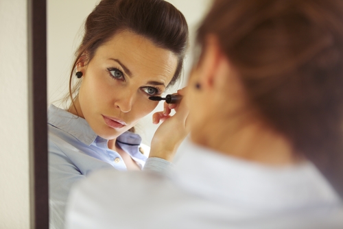 woman looking into mirror while applying makeup 
