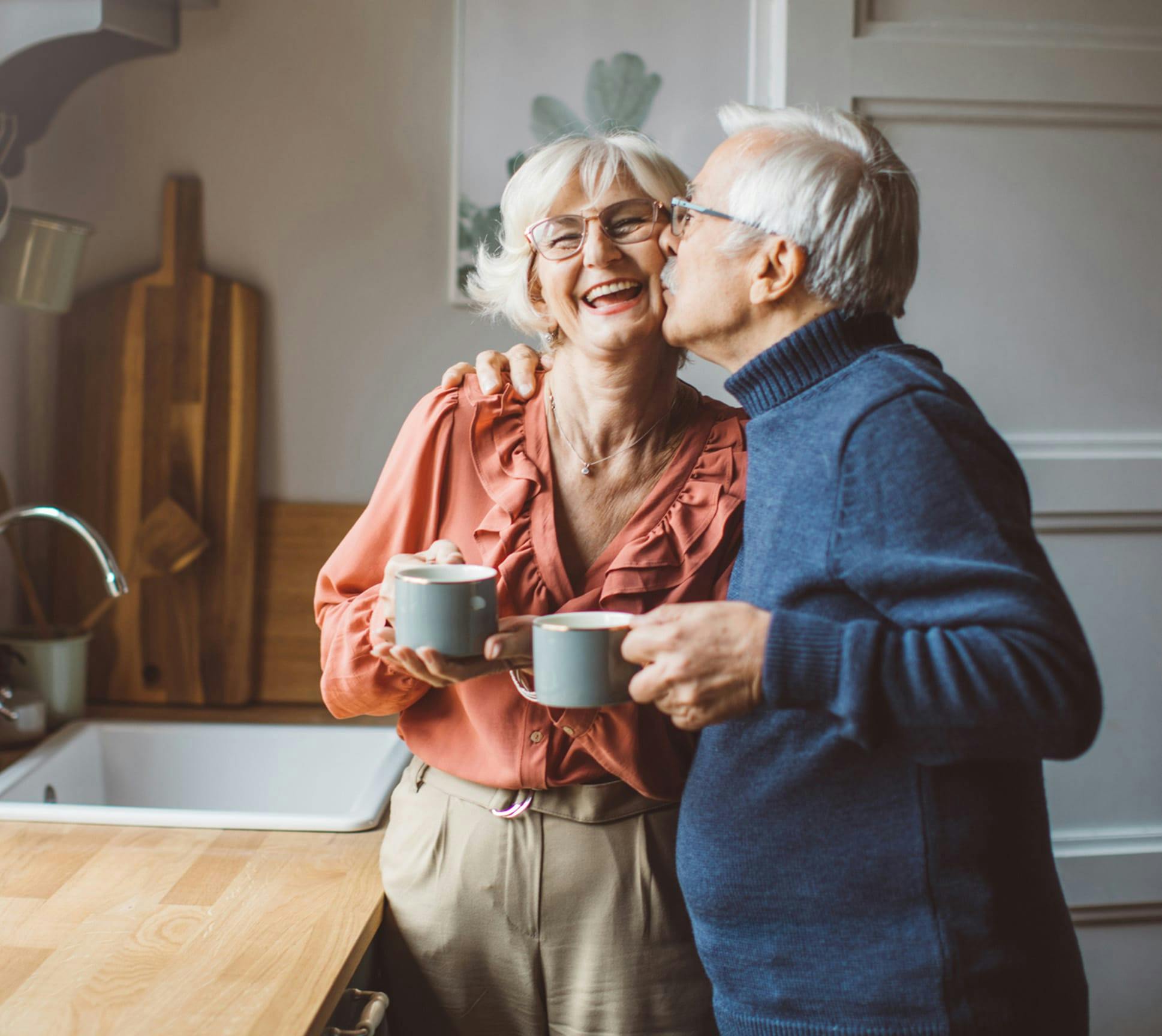 older man kissing woman on the cheek while holding coffee cups