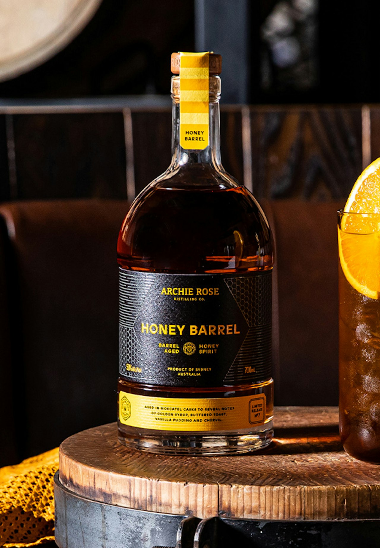 archie-rose-honey-barrel-aged-spirit-front-on-bottle-shot-with-cocktail-in-tall-glass-with-lemon-wedge
