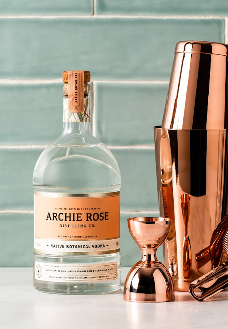 Archie-Rose-Native-Botanical-Vodka-with-copper-Toby-Shaker-copper-Hawthorn-strainer-and-graduated-copper-bell-jigger-sitting-on-a-bench