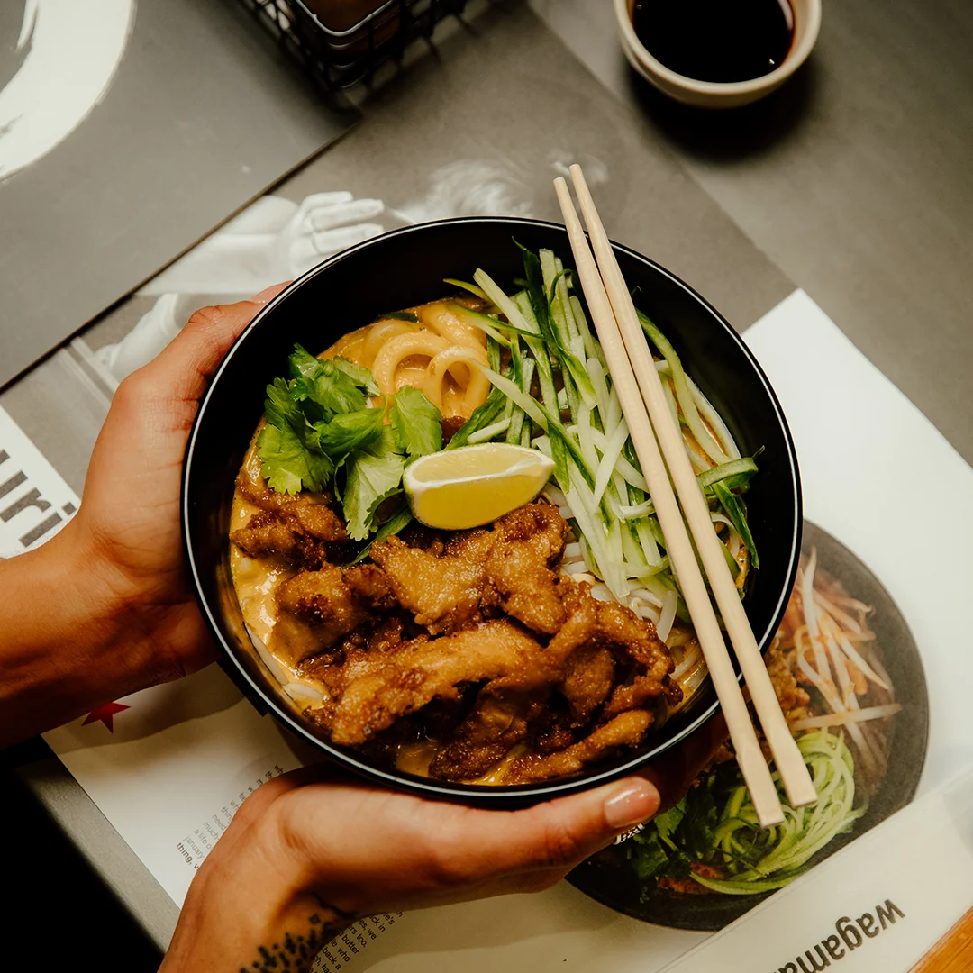 a bowl of vegan ramen with chopsticks being placed on a table with a wagamama menu