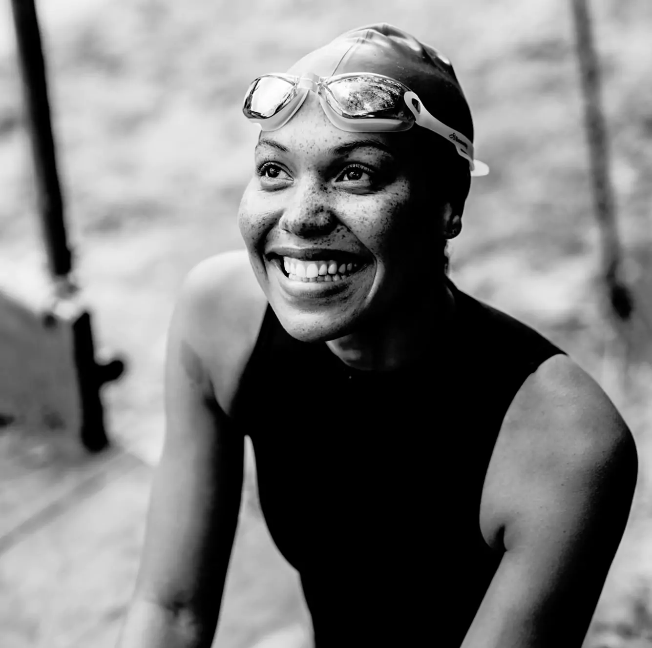 woman looking up and smiling wearing swimsuit, swimming hat and goggles