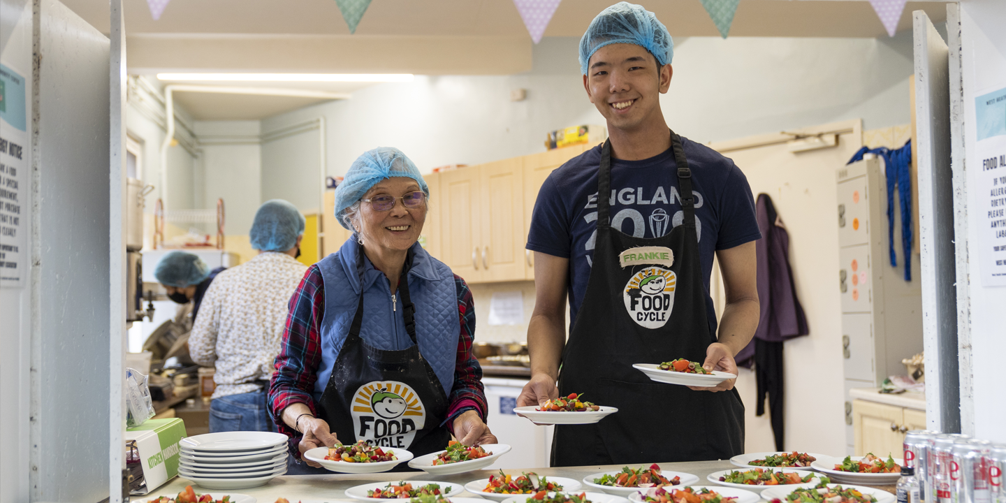 2 volunteers help serve food at FoodCycle west heath
