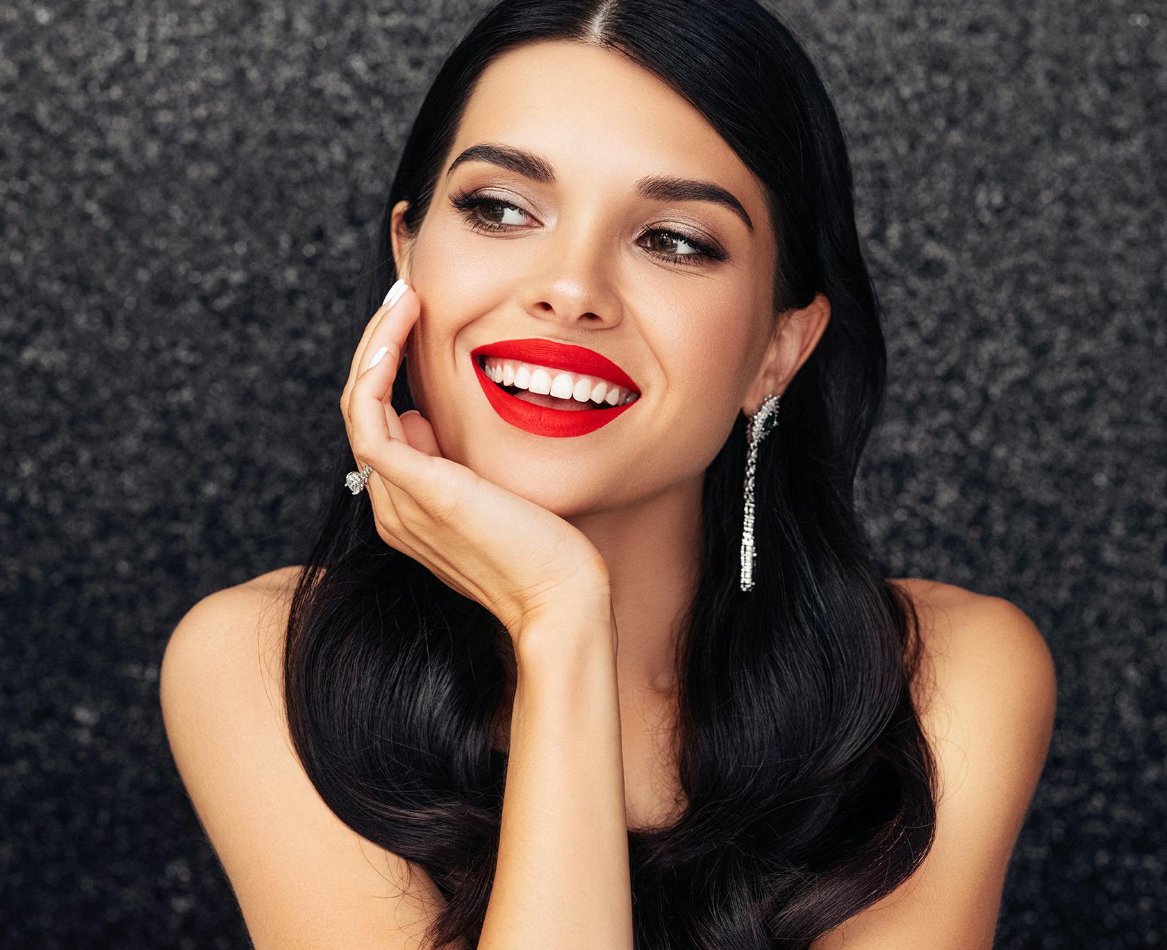 Woman with bright red lipstick and dangly earrings smiling