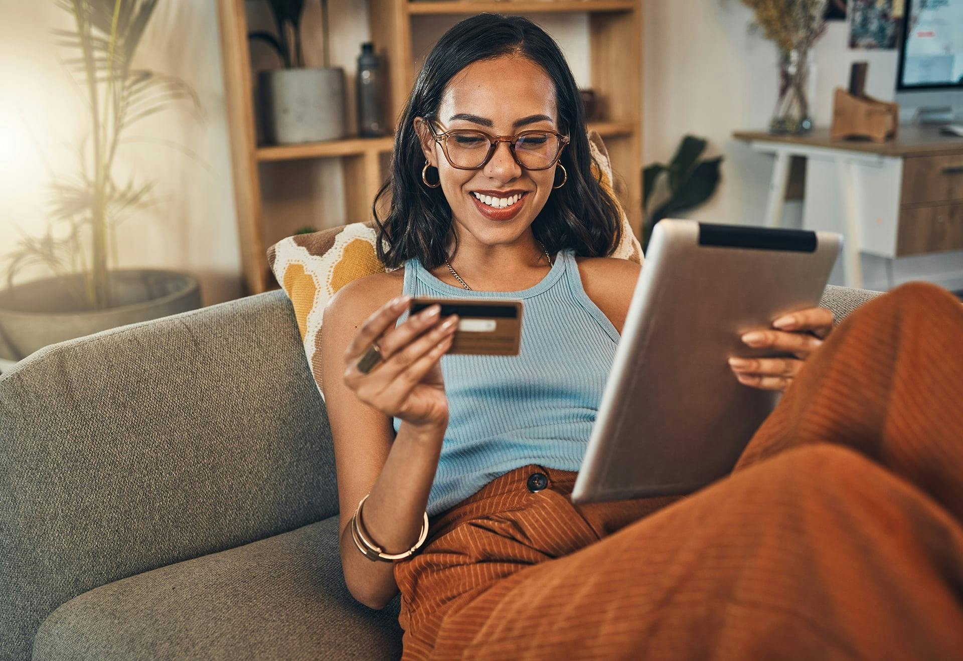 Woman holding a tablet and a credit card while sitting on a couch