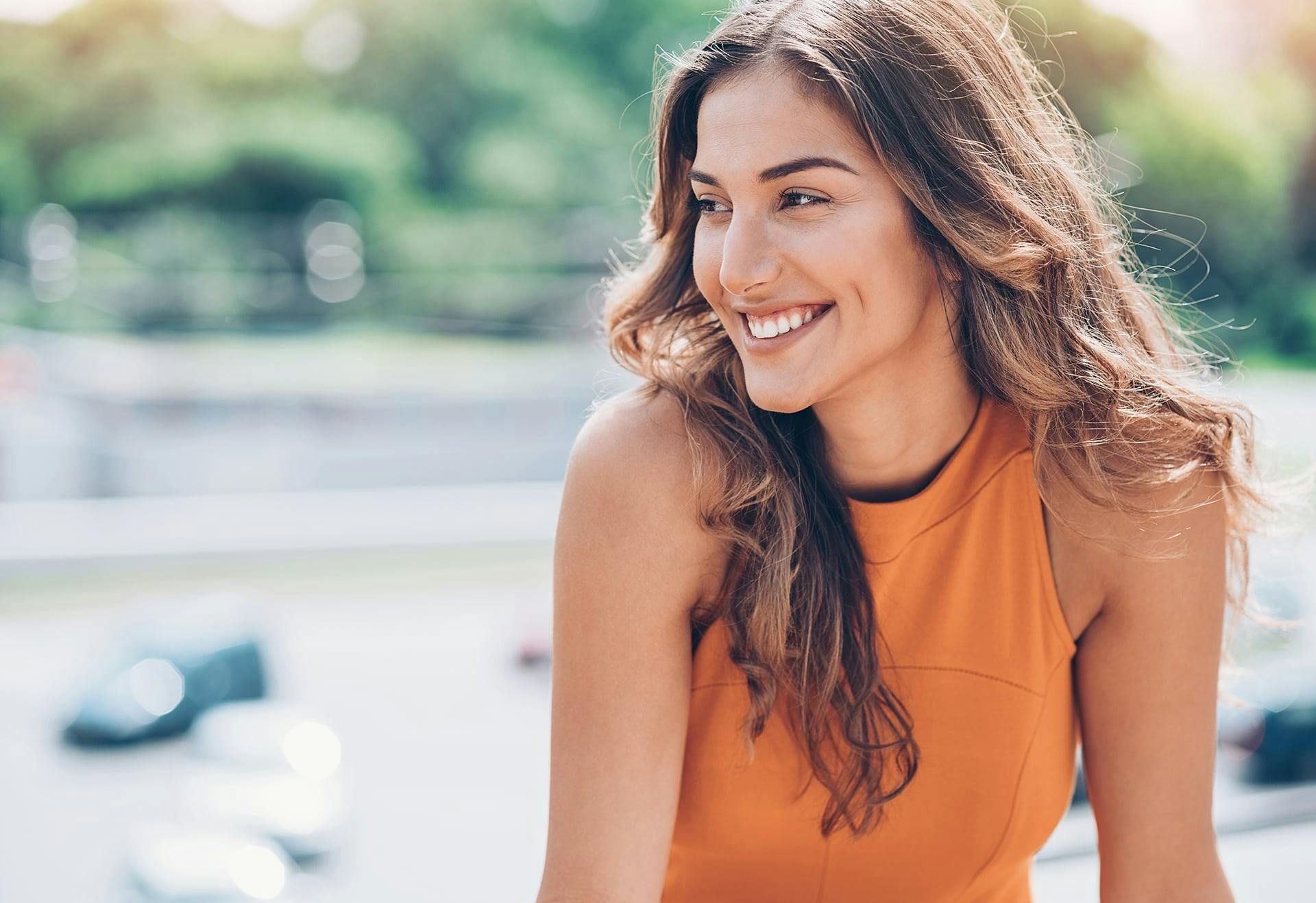 Woman in an orange top, looking to the sie and smiling