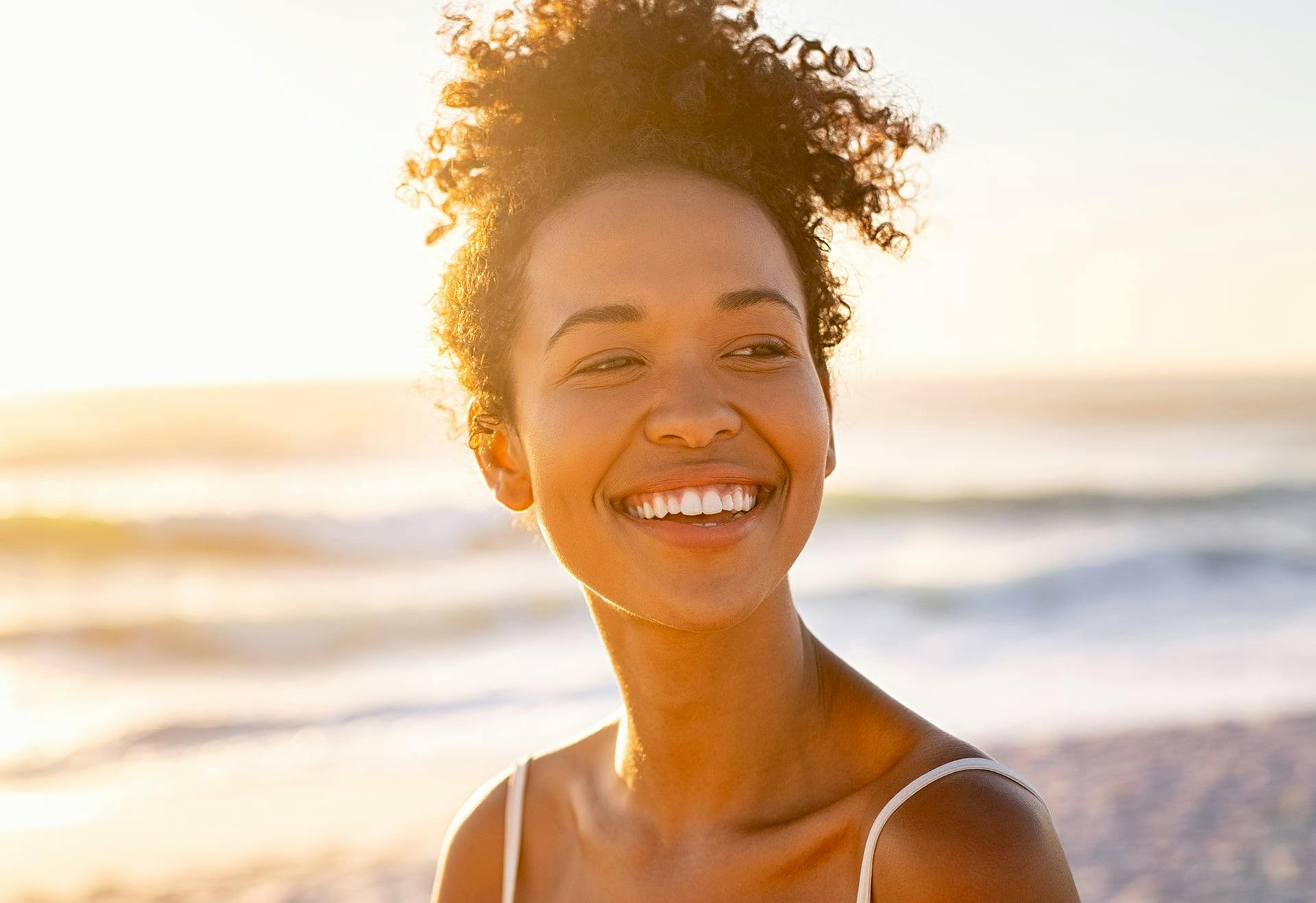 Woman with curly hair, smiling on the beach