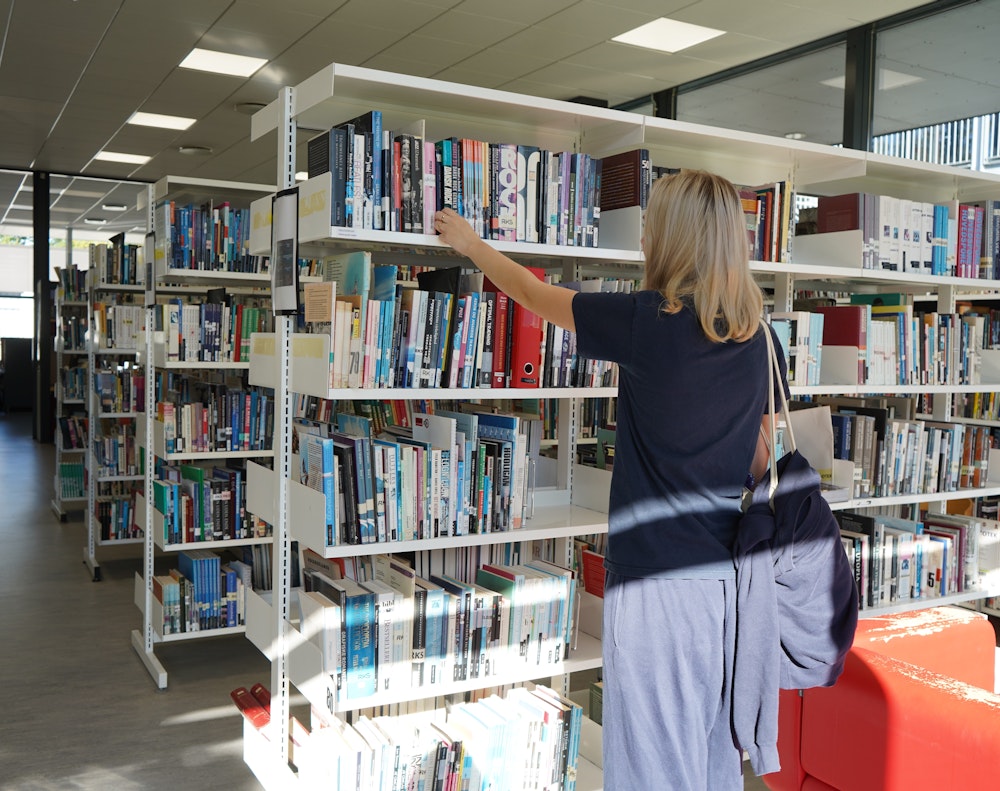 en pige tager en bog på bibliotekets hylde