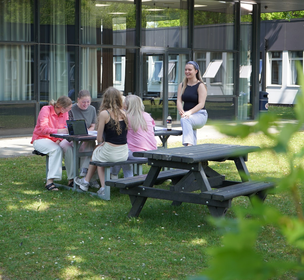 Elever sidder og samarbejder ved bord i gymnasiets atriumgård