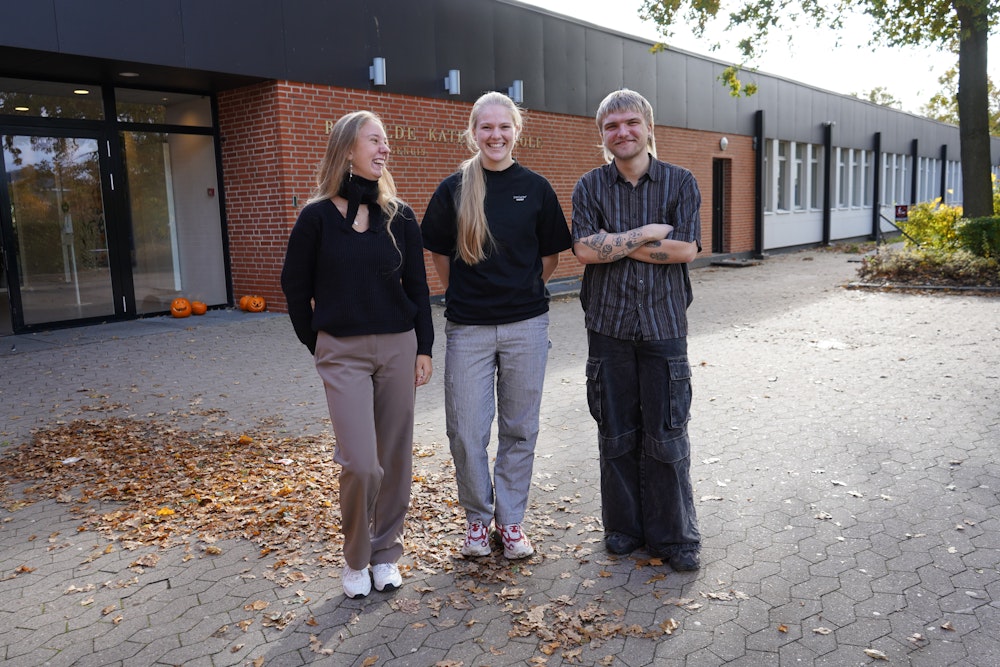 Tre 3.g'ere står ved hovedindgangen og smiler