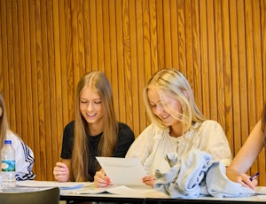 to elever i et klasselokale sidder sammen og kigger på en opgave