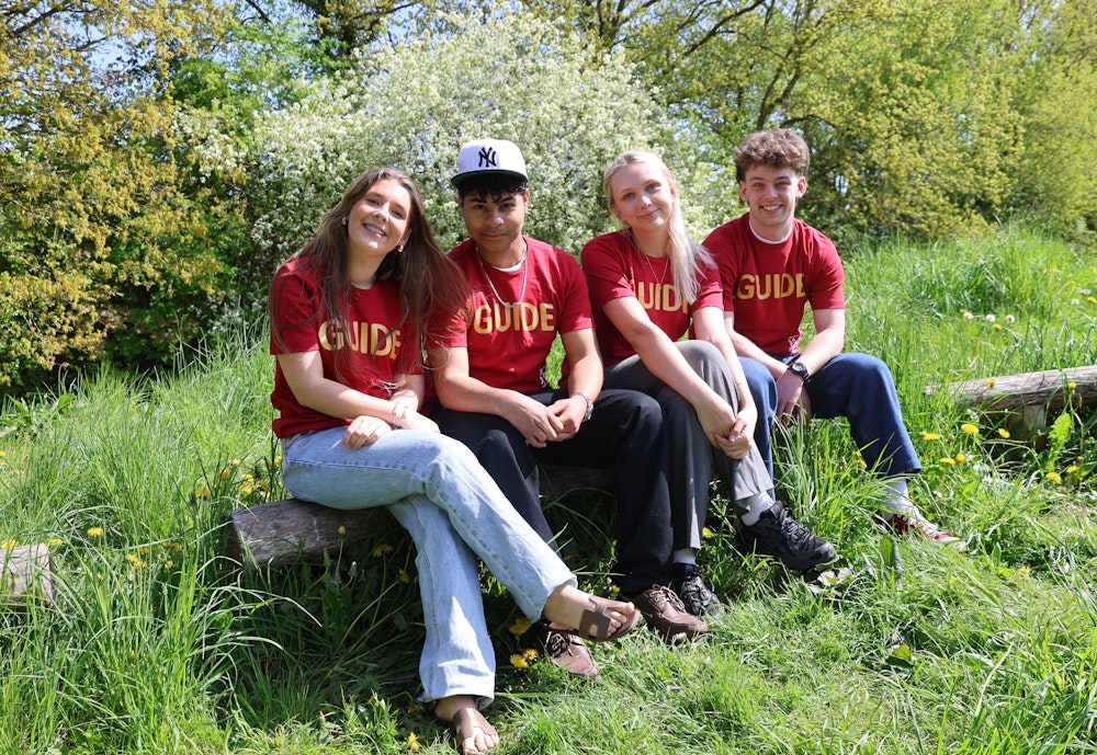 Fire elever i guide-T-shirts sidder sammen i det grønne og smiler til kameraet