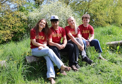 Fire elever i guide-T-shirts sidder sammen i det grønne og smiler til kameraet