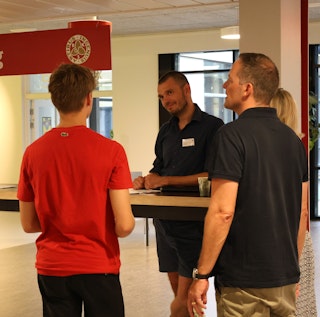 En studievejleder står ved et bord og lytter til en elev og elevens forældre