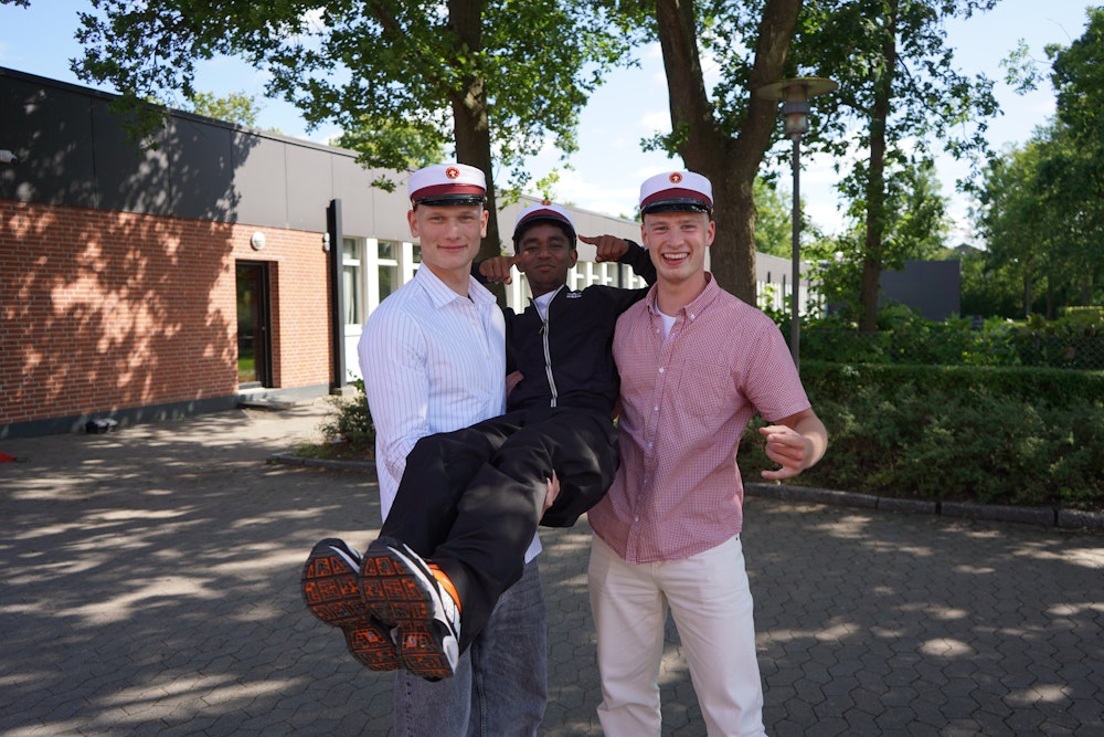 To studenter fra løfter deres ven  efter at have fået studenterhue på - årgang 2024-25