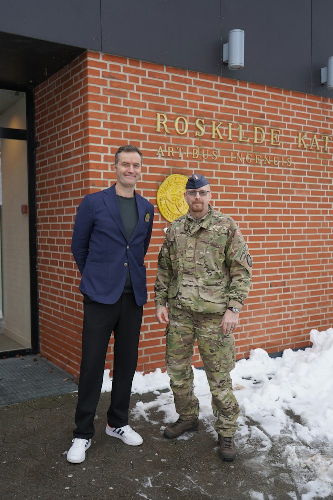 Rektor Thomas står foran skolen logo med Thomas Ravn fra Forsvaret