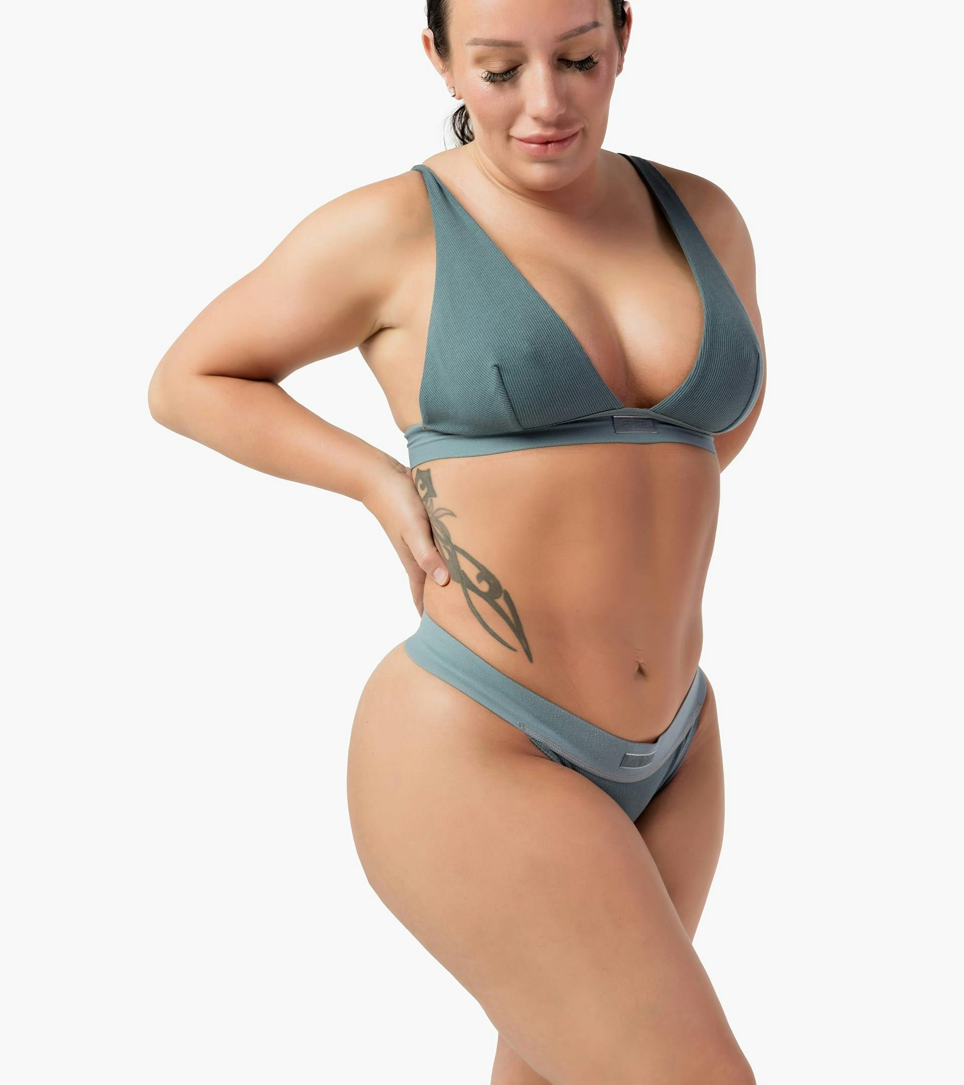 a woman in a turquoise bra top and underwear with a tattoo on her side posing for camera