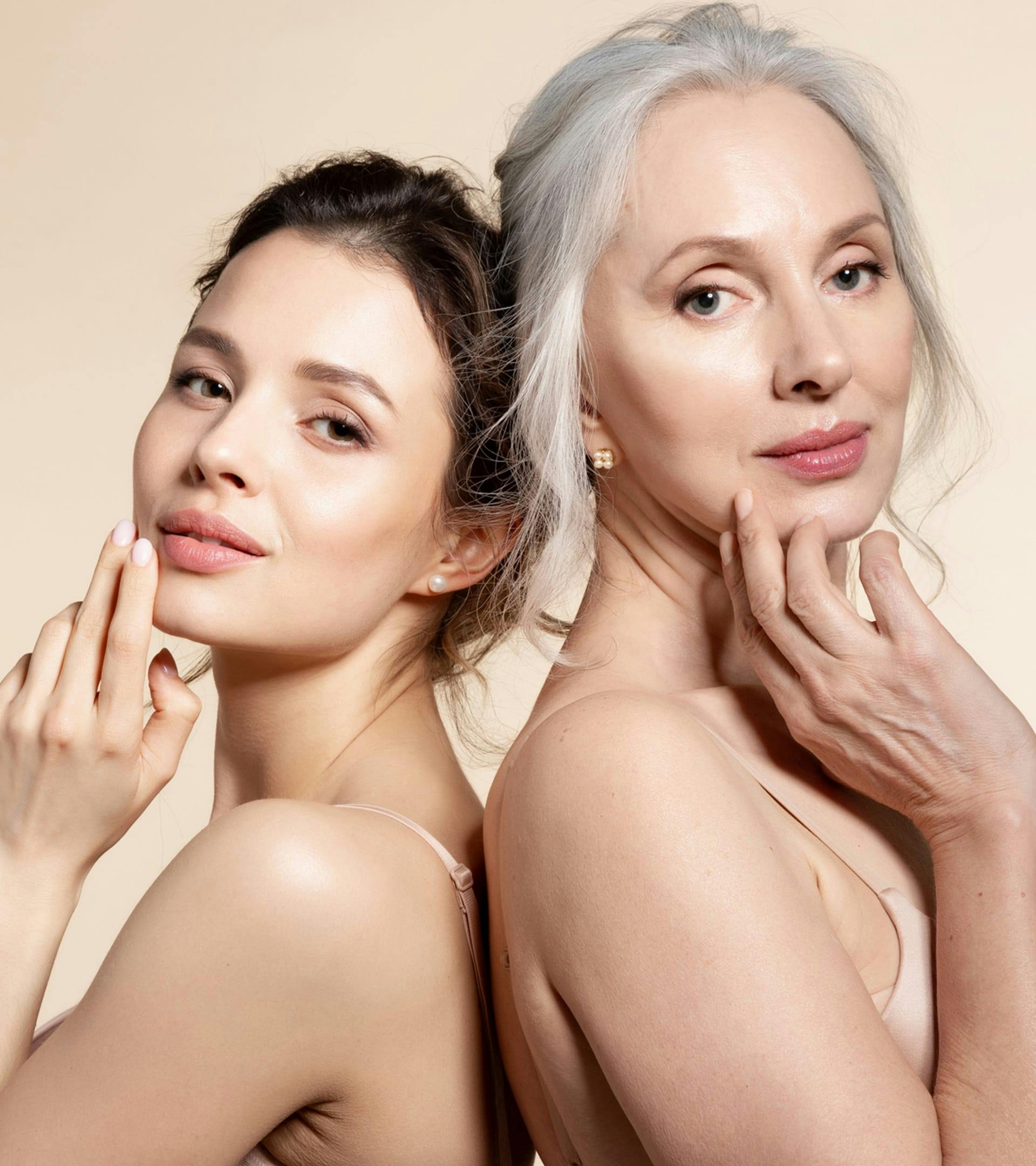 close up of older woman back to back with a younger woman posting for the camera in nude colored bra tops