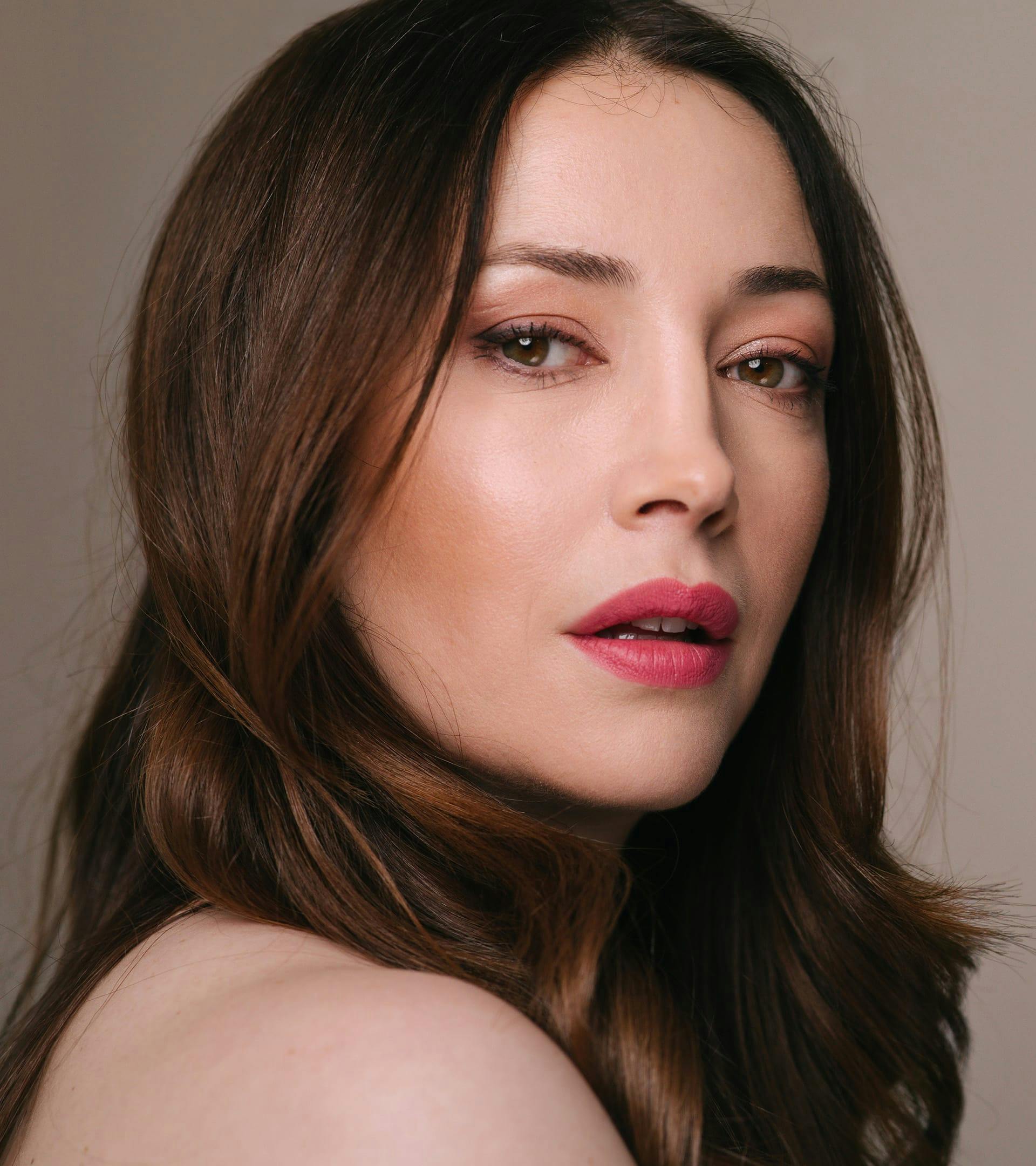 close up of a woman with long hair and a pink lipstick posing for the camera