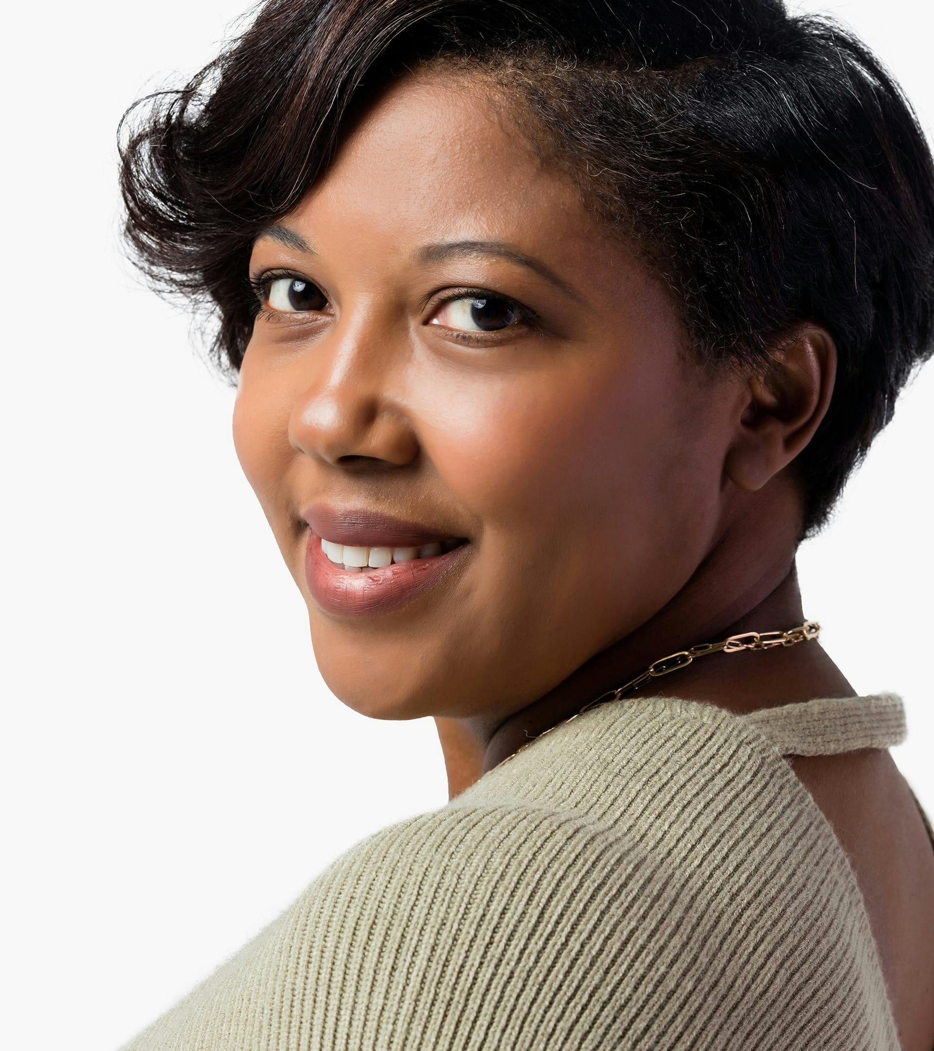 close up of woman with short black hair and a tan sweater smiling at camera