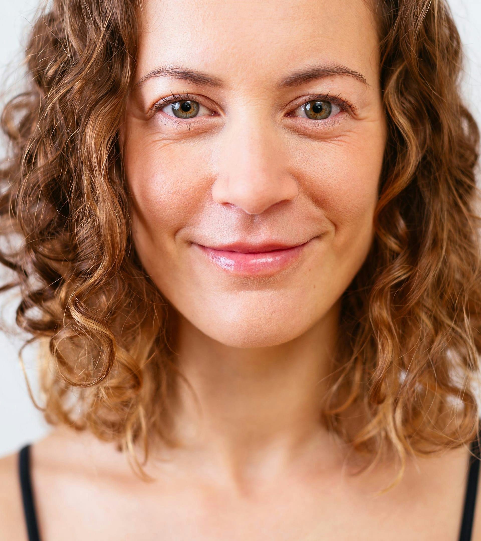 close up of woman with curly hair and a black top smiling for camera