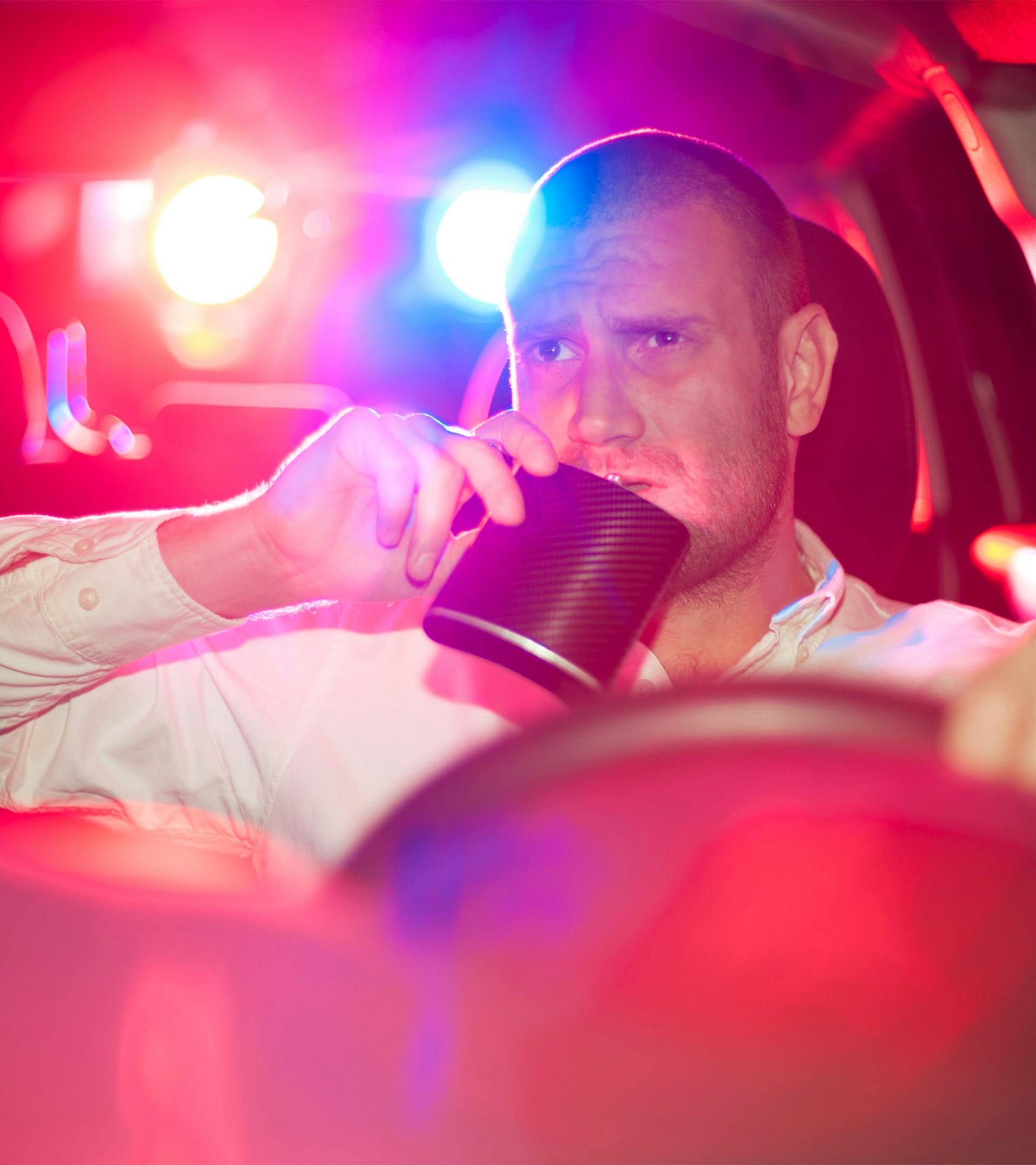 Man drinking from a flask in the drivers seat of a car.