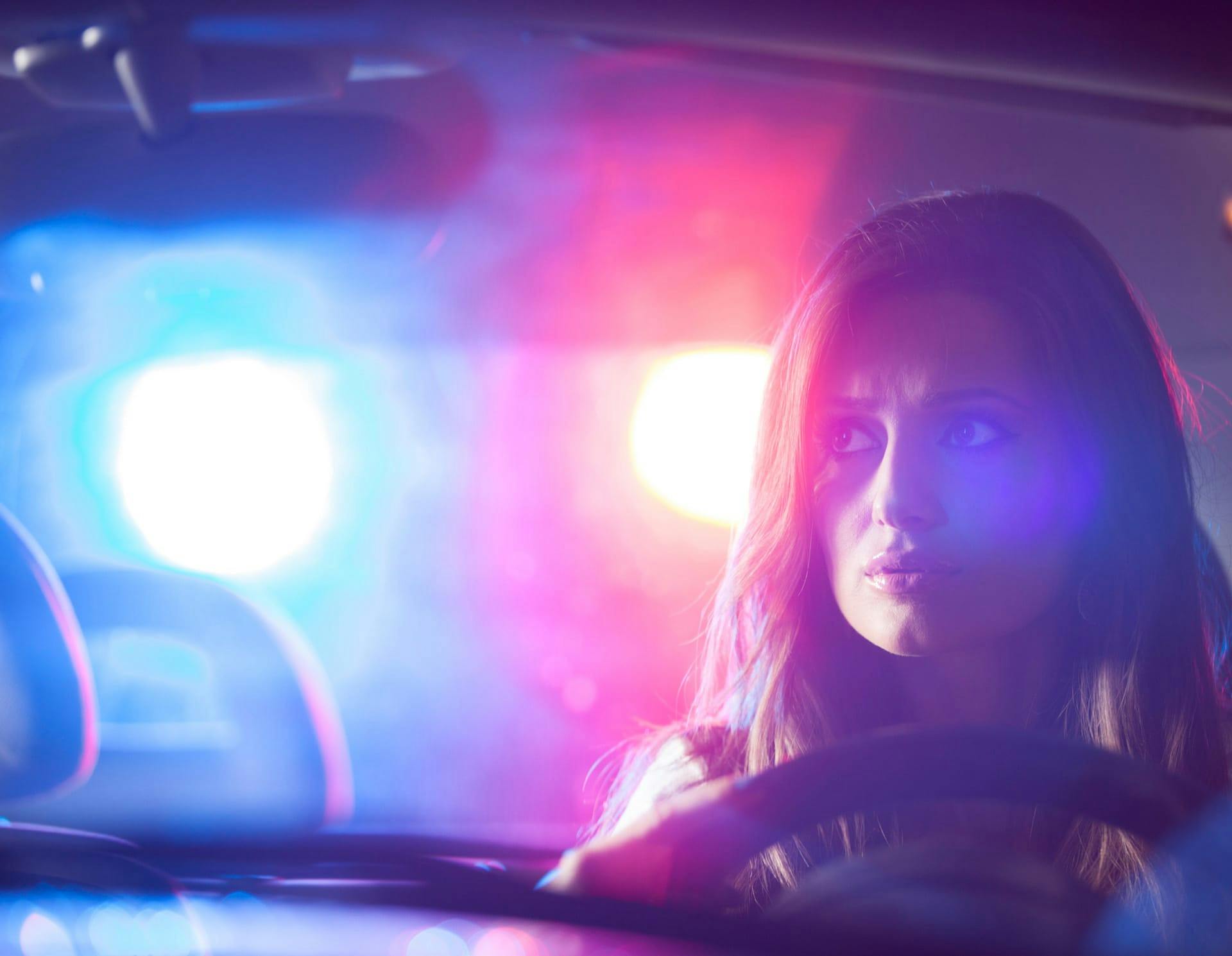 Woman in car with police lights in the background