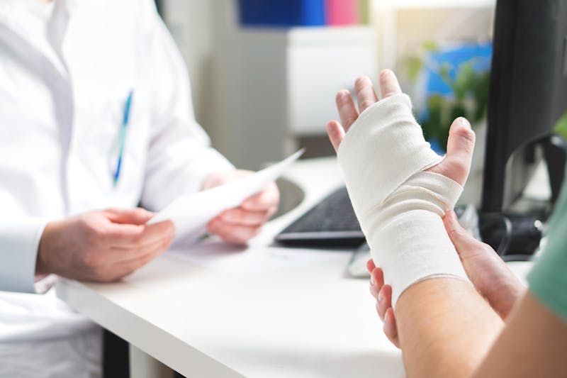 Closeup of a bandaged hand and a doctor sitting across the table.