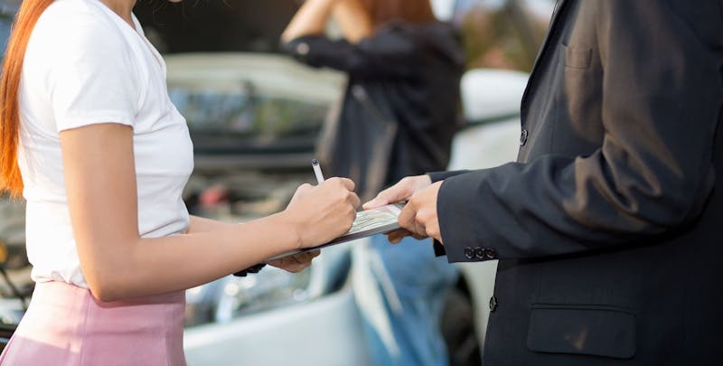 Woman signing something with a car accident in the background.