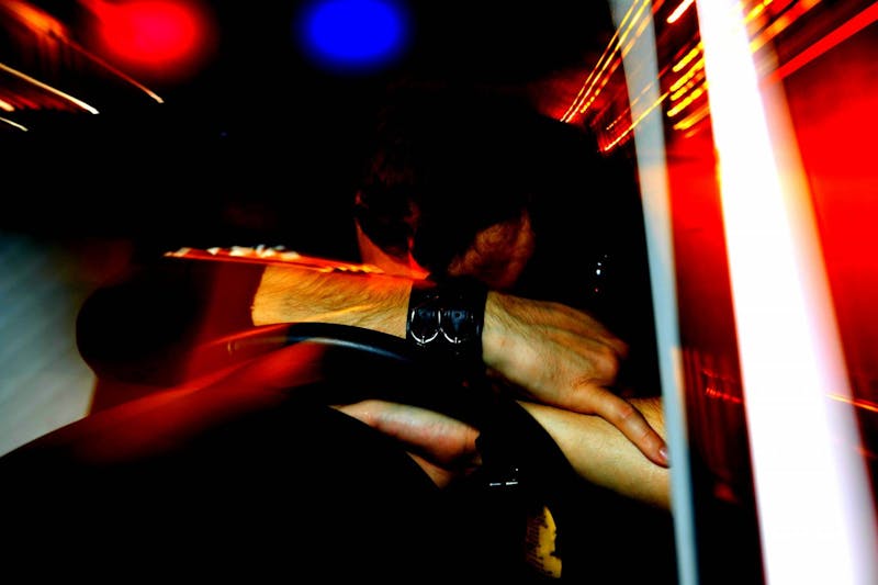Blurred photo of a man resting his head on a steering wheel in distress.