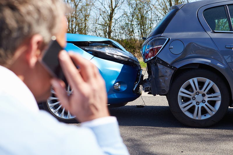 Man talking on phone in front of car crash.