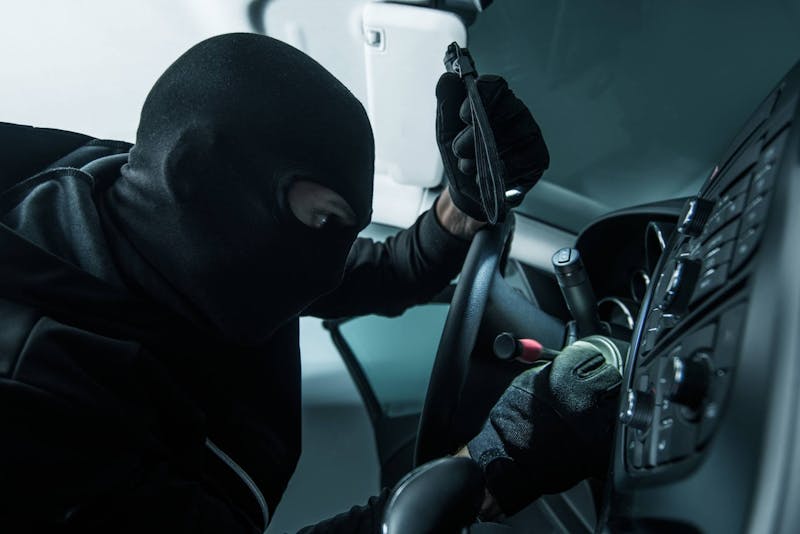 Criminal in a mask breaking into a car.
