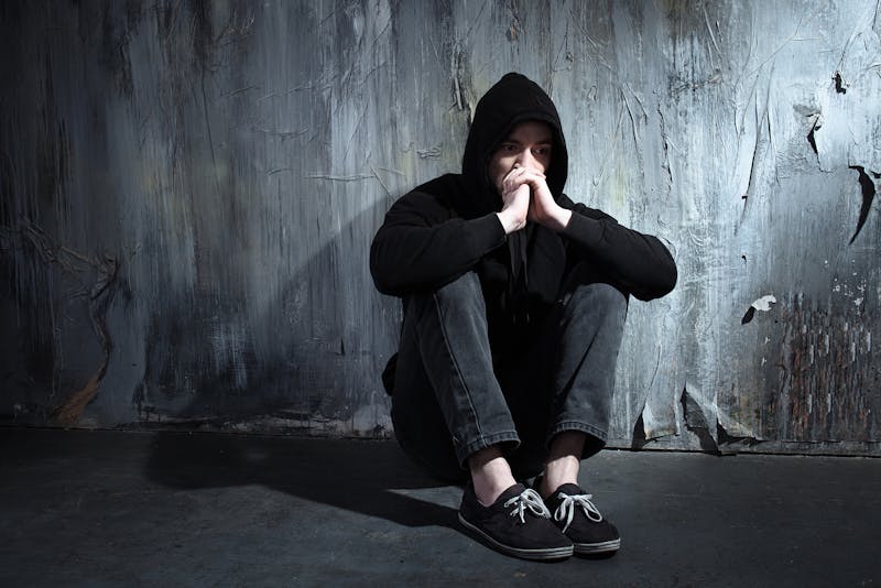 Person in a hoodie sitting on the ground looking distressed.
