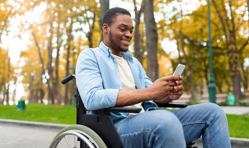 Man outside in a wheelchair looking at his phone smiling.