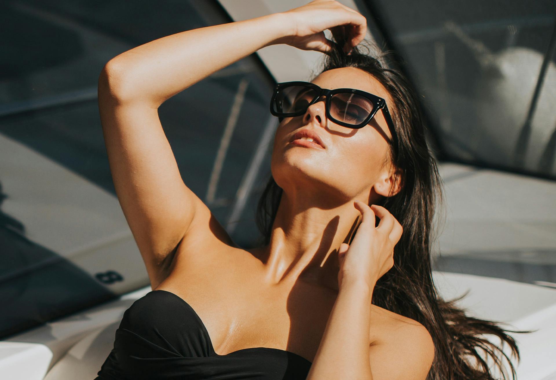 Woman leaning her head back wearing black sunglasses and bathing suit