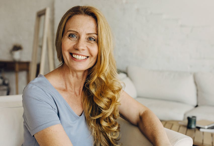 Woman with long blonde curly hair sitting down and smiling