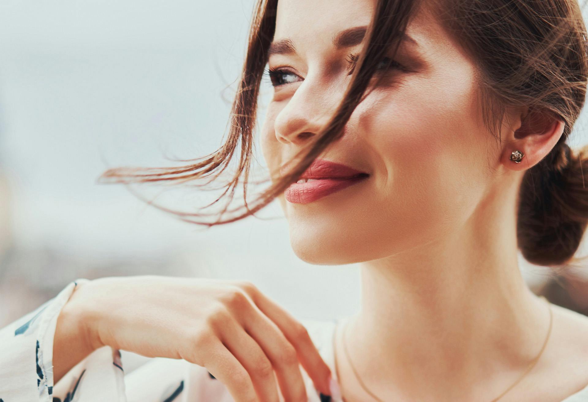 Woman with full lips outside with her bangs blowing in her face