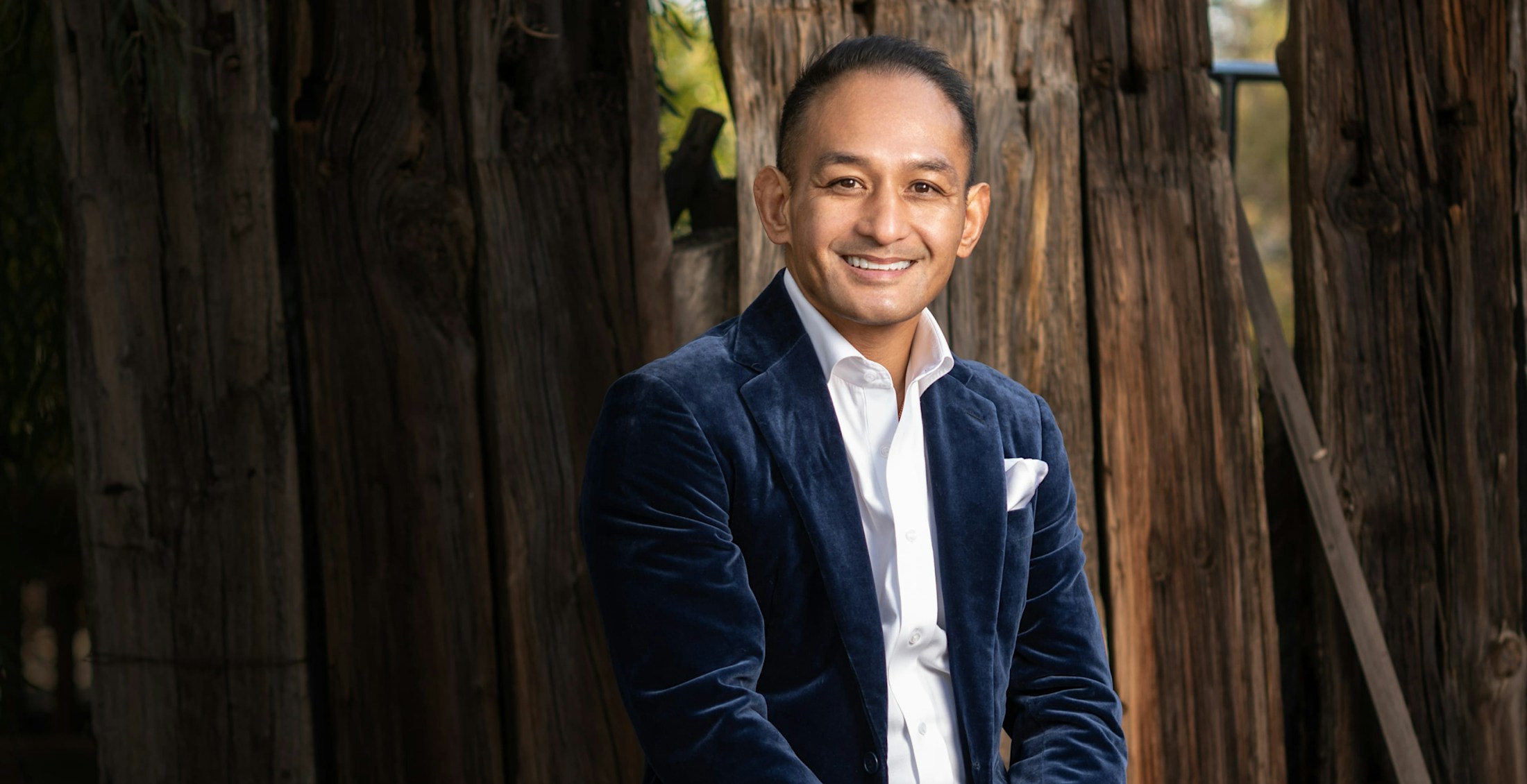 Dr. Andres in a suit in front of a wooden fence