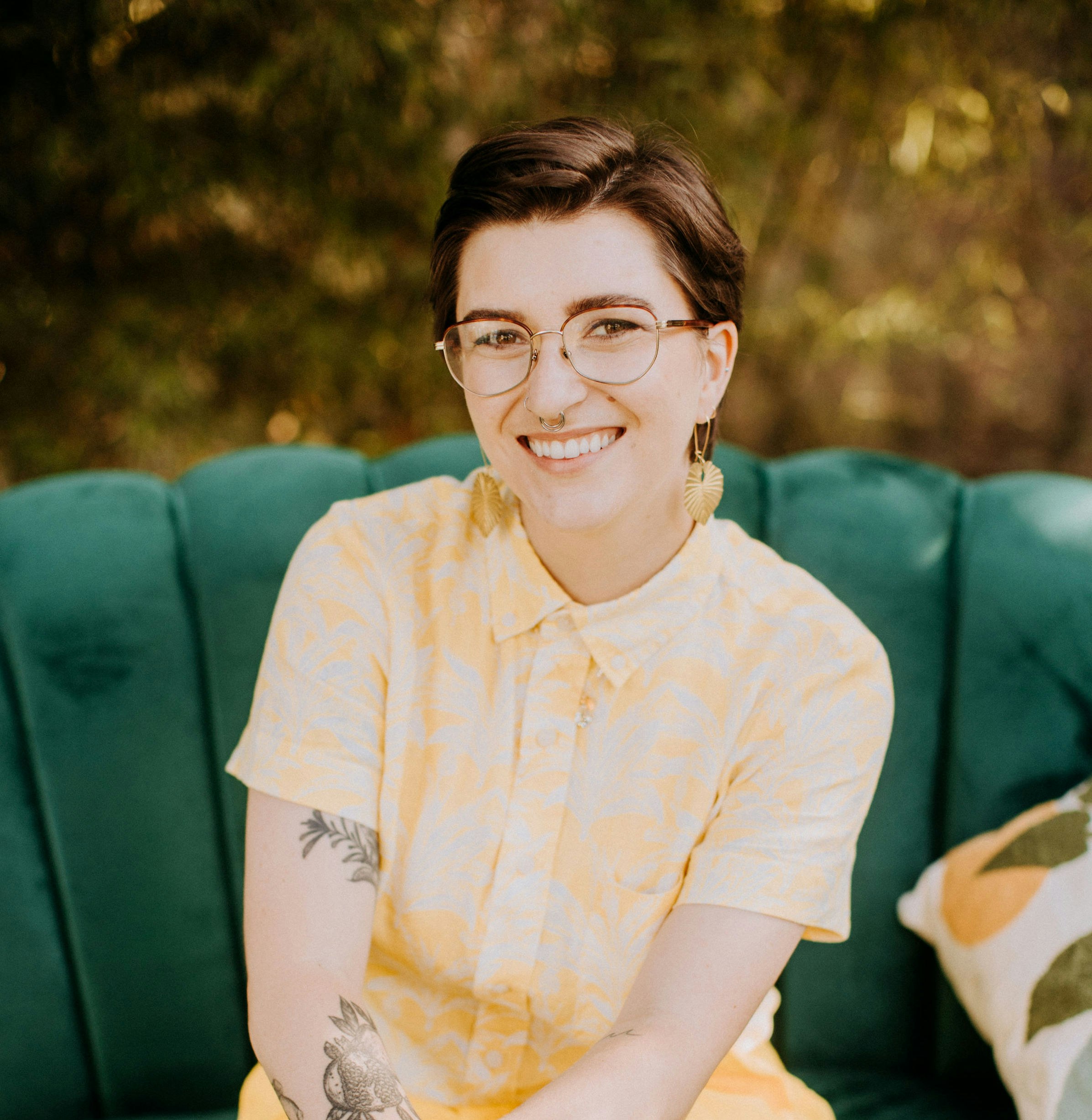 Erica wearing a yellow outfit sitting on a green velvet couch smiling at the camera.