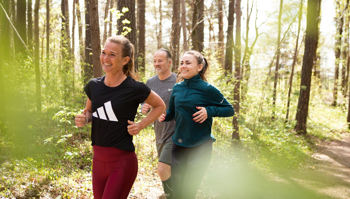 Tre av Midagons medarbetare tränar tillsammans i skogen. De joggar fram på ett stig och ler.