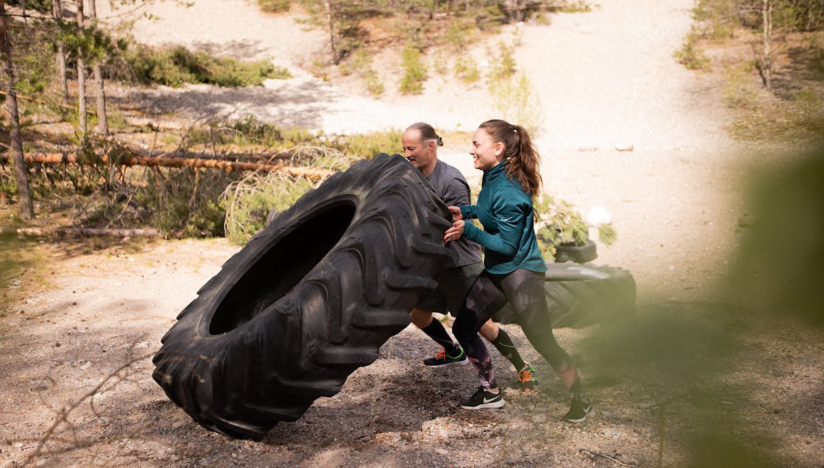 Två av Midagons medarbetare tränar på ett utegym. De puttar på ett stort traktordäck tillsammans.