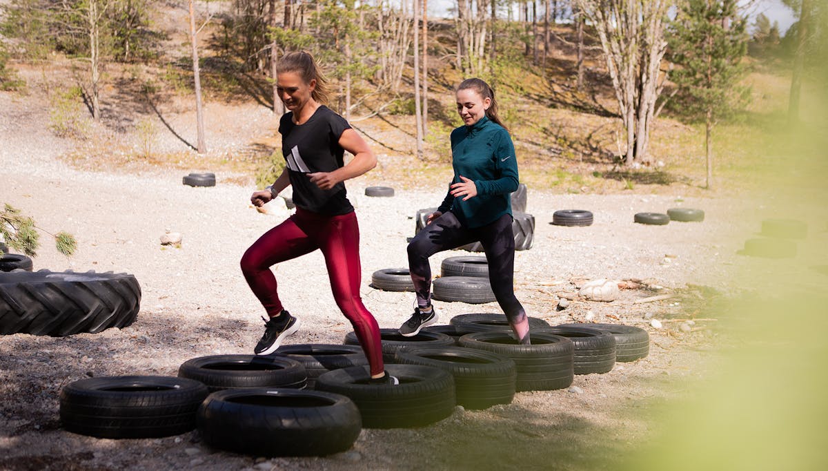 Två av Midagons medarbetare tränar i ett utegym. De springer i bildäck som ligger utplacerade i två rader på marken.