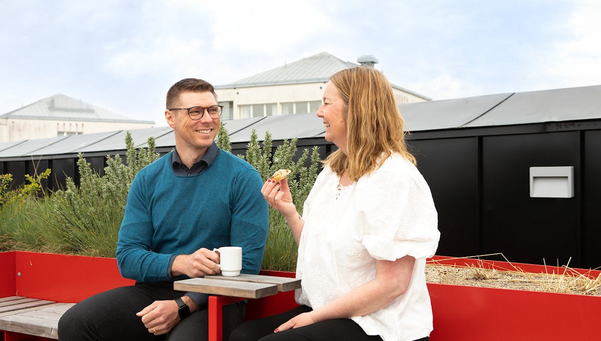 Två kollegor fikar med kaffe och bulle på takterrassen på Midagons Örebrokontor.