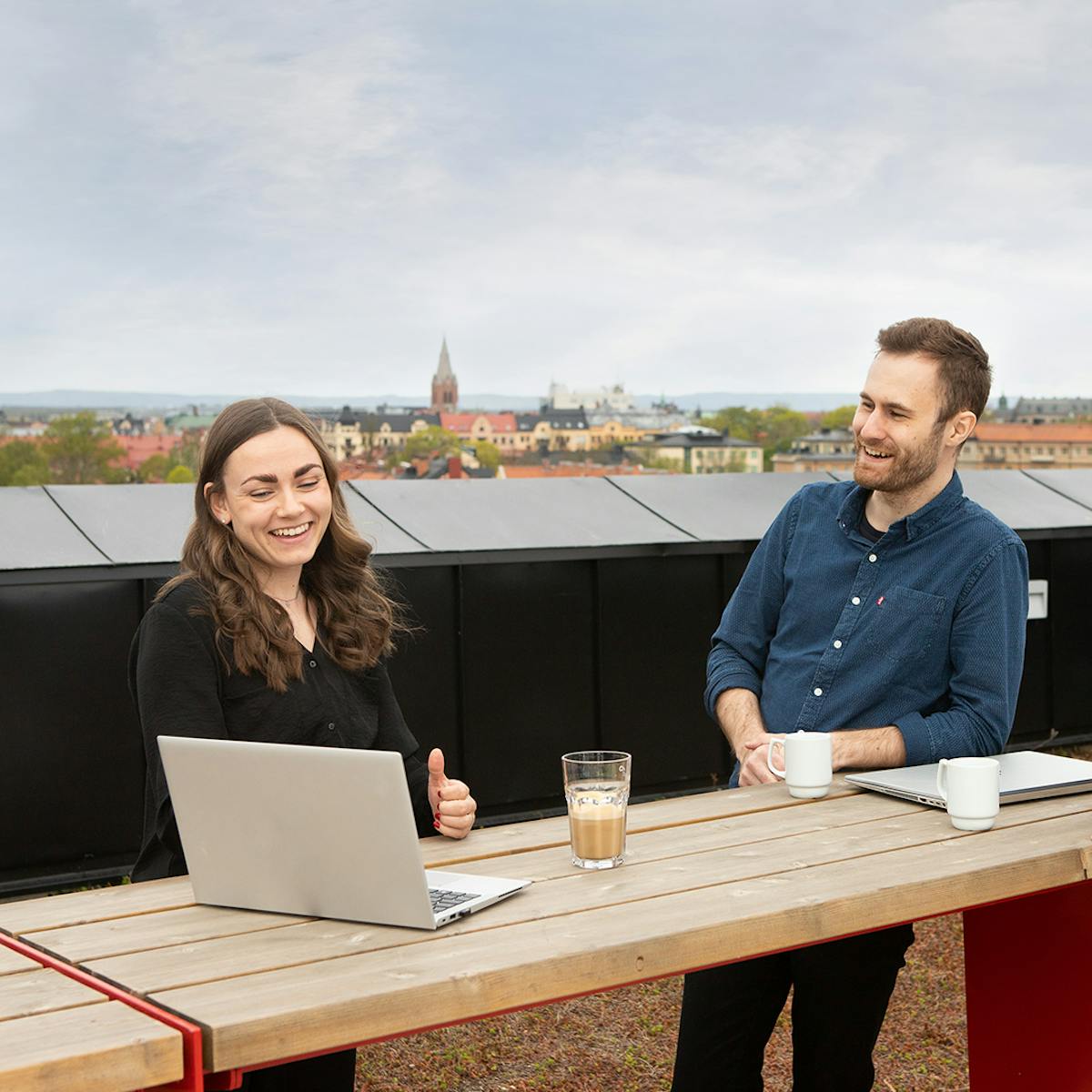 Två kollegor står vid ett ståbord på takterrassen på Midagons Örebrokontor. På bordet står kaffekoppar och en varsin dator.