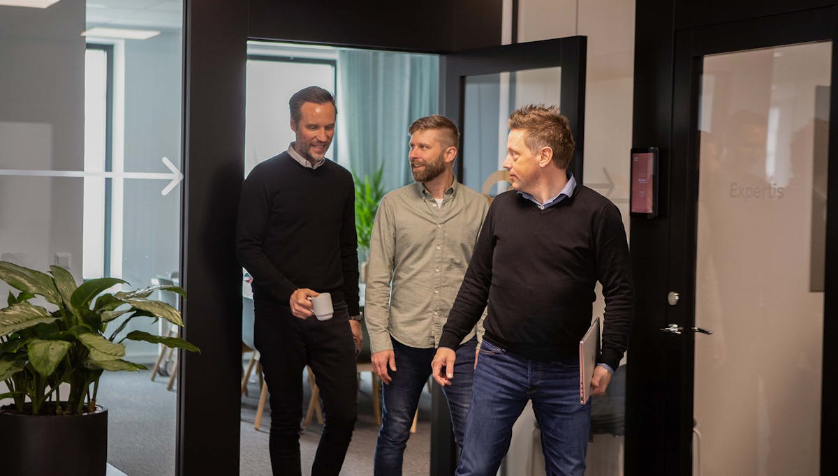 Tre kollegor på språng på Örebrokontoret. En har en kaffekopp i handen och en bär på sin dator.