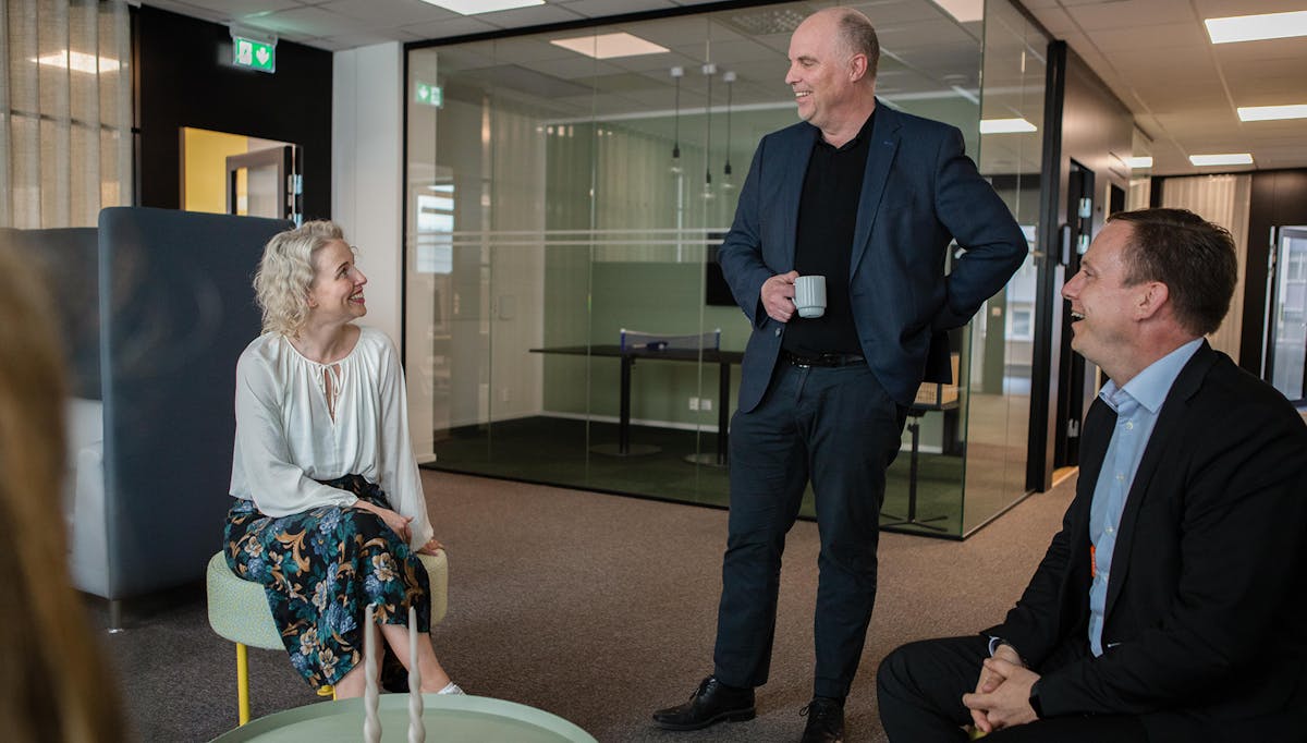 Tre kollegor på Örebrokontoret som tar en paus i arbetet. En dricker kaffe och de ler mot varandra.