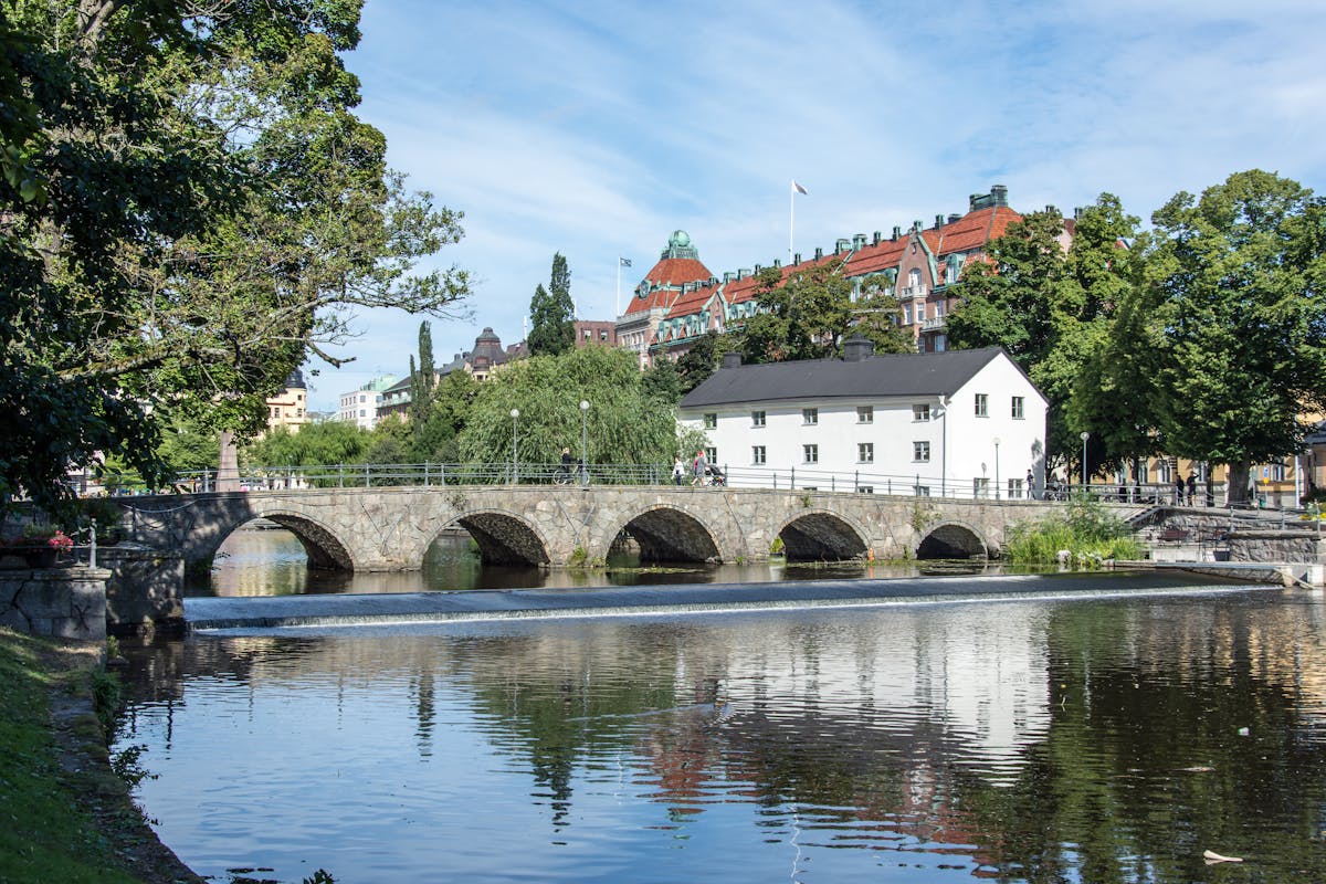 Vy över bro i Örebro en varm sommardag. I bild en stenbro, vitt hus, vatten och Midagon Sveriges huvudkontor.